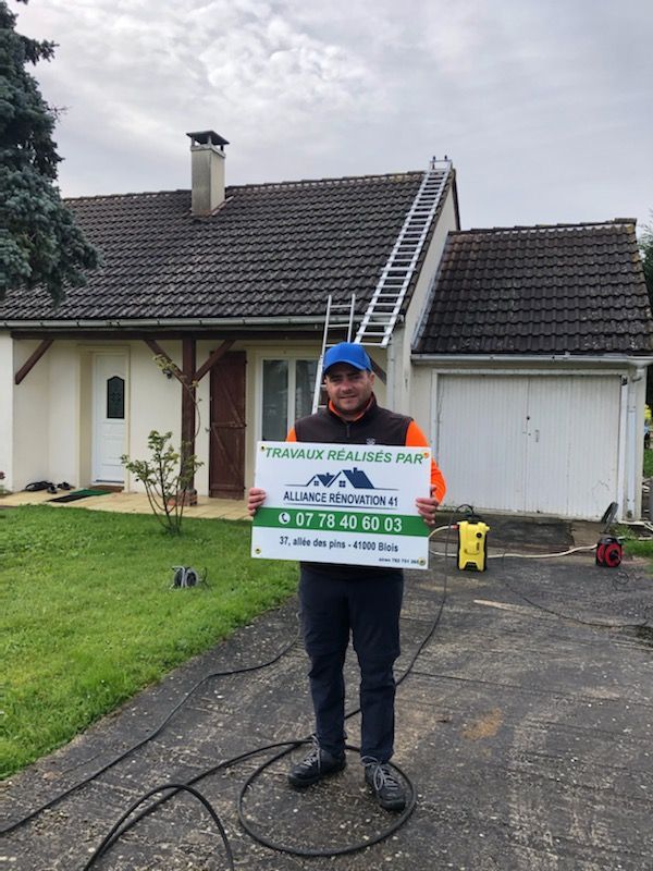 Employé de l'entreprise tenant une pancarte publicitaire devant une maison avec toiture en ardoise