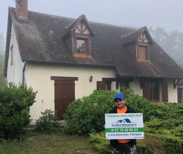 Employé d'alliance rénovation 41 devant une maison tenant une pancarte publicitaire