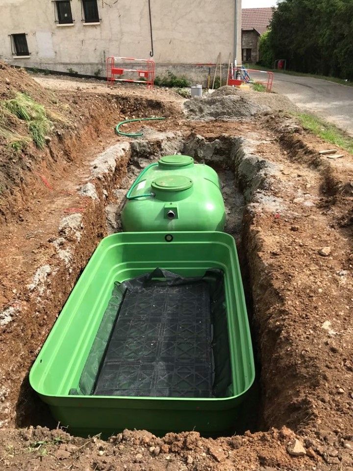 Un réservoir d'eau souterrain écologique est installé dans une tranchée de terre à côté d'un bâtiment.