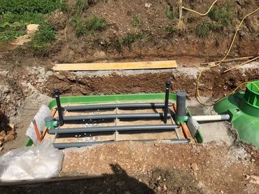 Chantier de construction avec une échelle métallique verte au-dessus d'une tranchée, à côté de terre et de bord en béton.