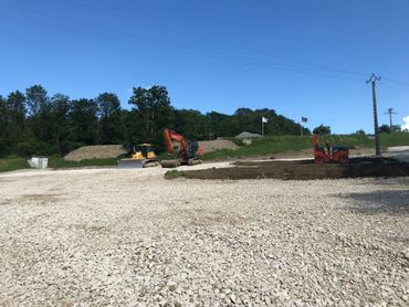 Chantier de construction avec une excavatrice et un camion rouge sur un terrain gravillonné sous un ciel bleu dégagé.