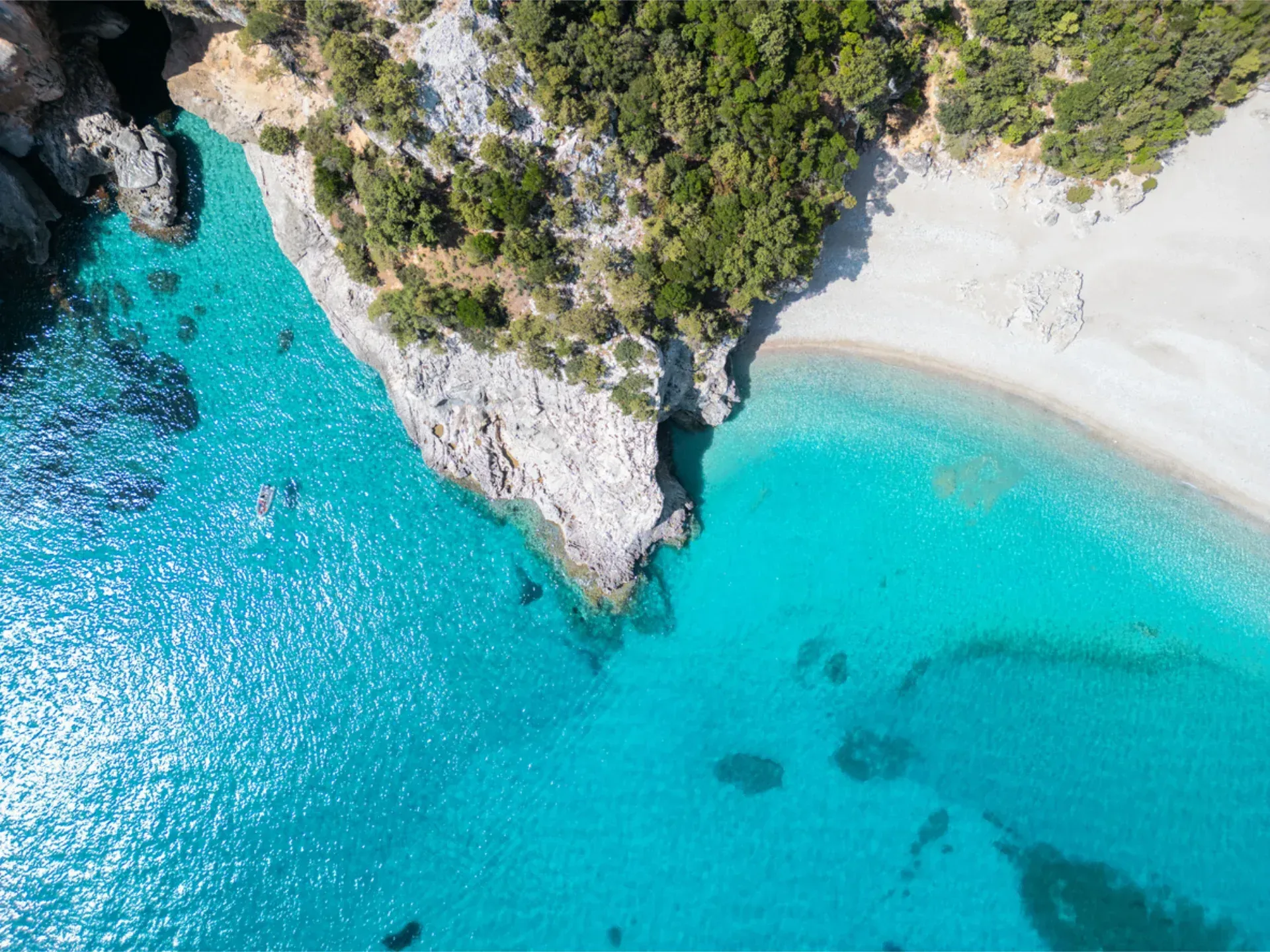 An aerial view of turquoise ocean waters meeting dramatic, rocky cliffs and a small white sand beach.