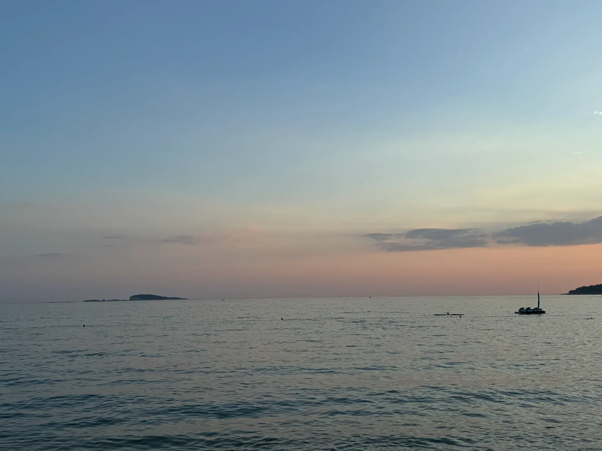 A tranquil sunset view over a calm sea with distant islands and a small boat on the horizon.