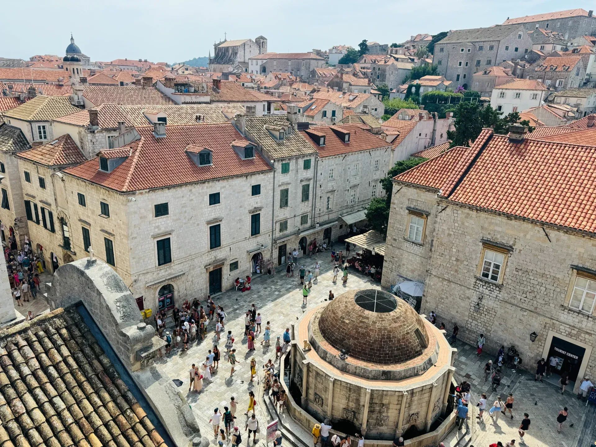 High-angle view of Onofrio’s Fountain in Dubrovnik, surrounded by crowds in a historic stone town with terracotta roofs.