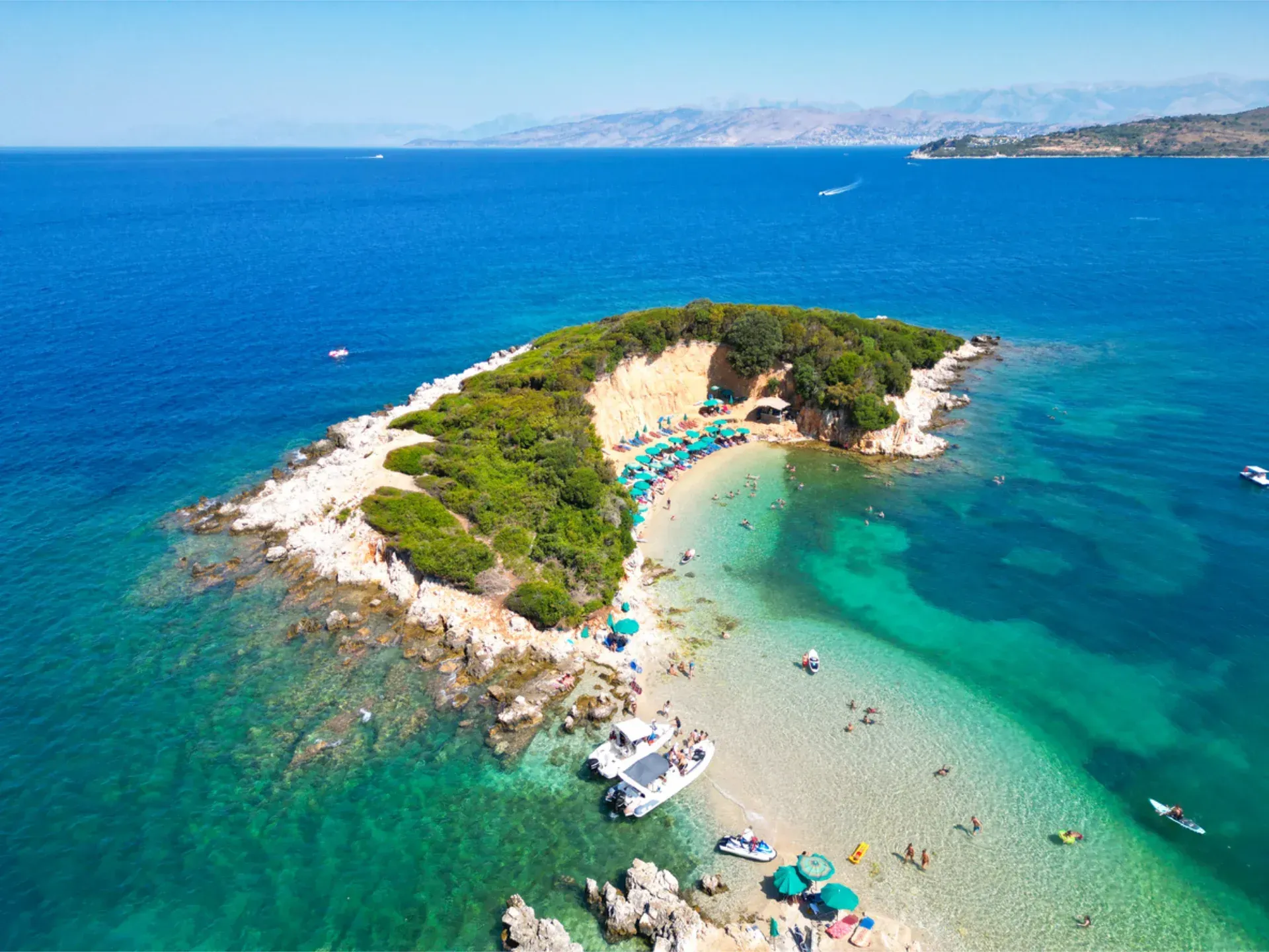 Straw beach umbrellas and wooden lounge chairs on a sandy beach overlooking a calm blue ocean under a clear sky.