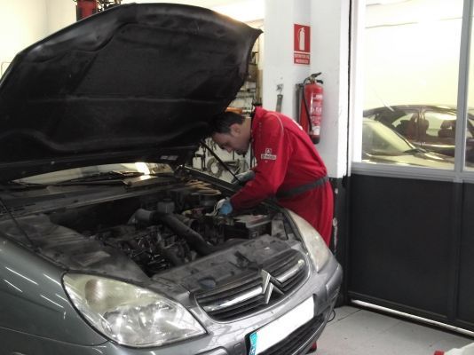 Un hombre está trabajando bajo el capó de un coche.