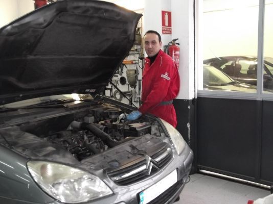 Un hombre está trabajando en un coche con el capó abierto.