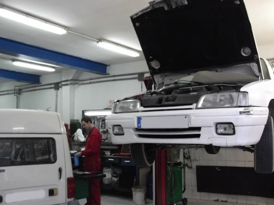 Un coche blanco con el capó levantado está en un elevador en un garaje.