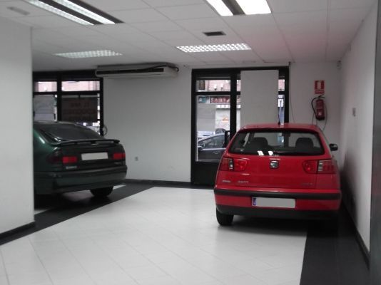 Un coche rojo está aparcado en un garaje al lado de un coche verde.