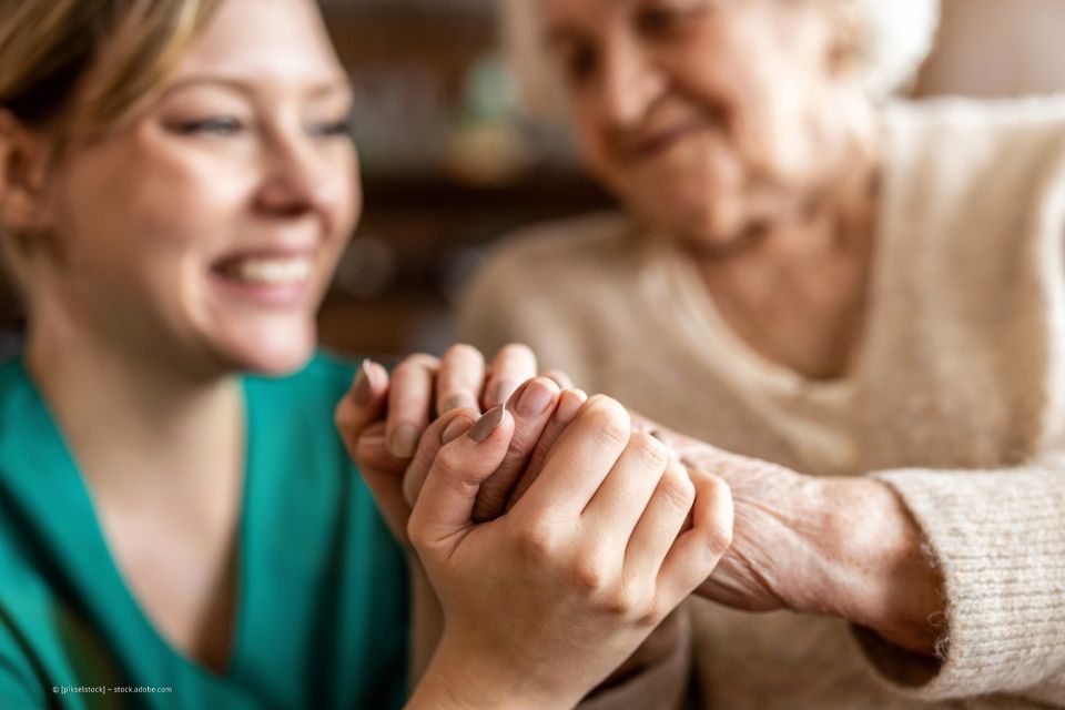 Pflegerin und Seniorin legen die Hände aufeinander