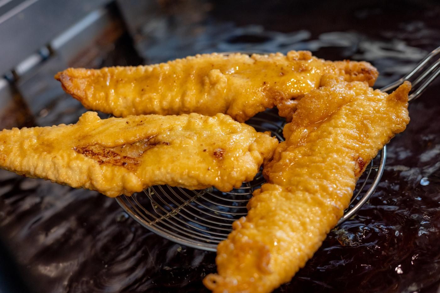 Drei Fischstücke werden in einer Fritteuse zubereitet.