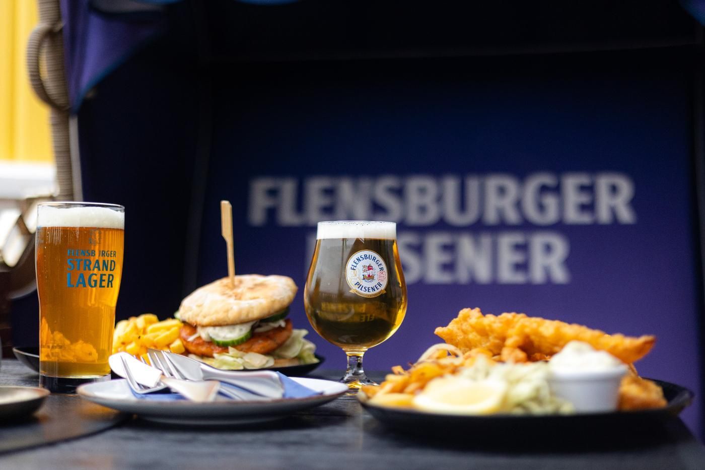 Ein Tisch mit Essen und Getränken vor einem Schild mit der Aufschrift „Flensburger Sener“