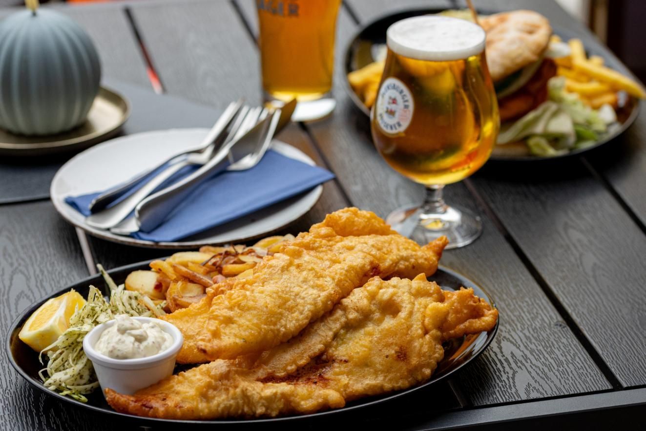 Auf einem Tisch steht neben einem Glas Bier ein Teller mit Fish and Chips.