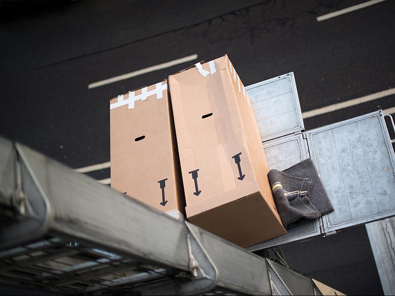 Deux boîtes en carton sur un tapis roulant métallique, légèrement inclinées sur un fond d'asphalte sombre.