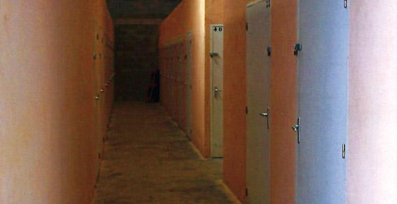 Couloir étroit aux murs couleur pêche et aux casiers métalliques. Sombre au fond.