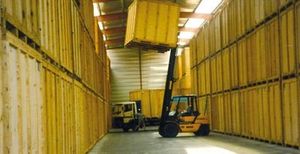 Un chariot élévateur soulève une caisse jaune dans un entrepôt rempli de conteneurs de stockage en bois.