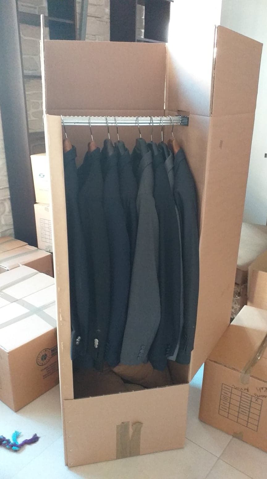 Boîte penderie en carton avec vêtements suspendus à l'intérieur.