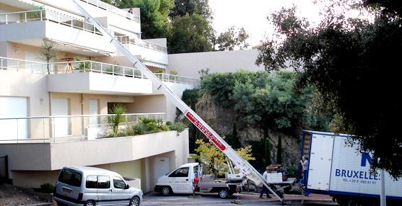 Un camion de déménagement soulève des meubles jusqu'à un bâtiment. Un bras se déploie vers le haut.