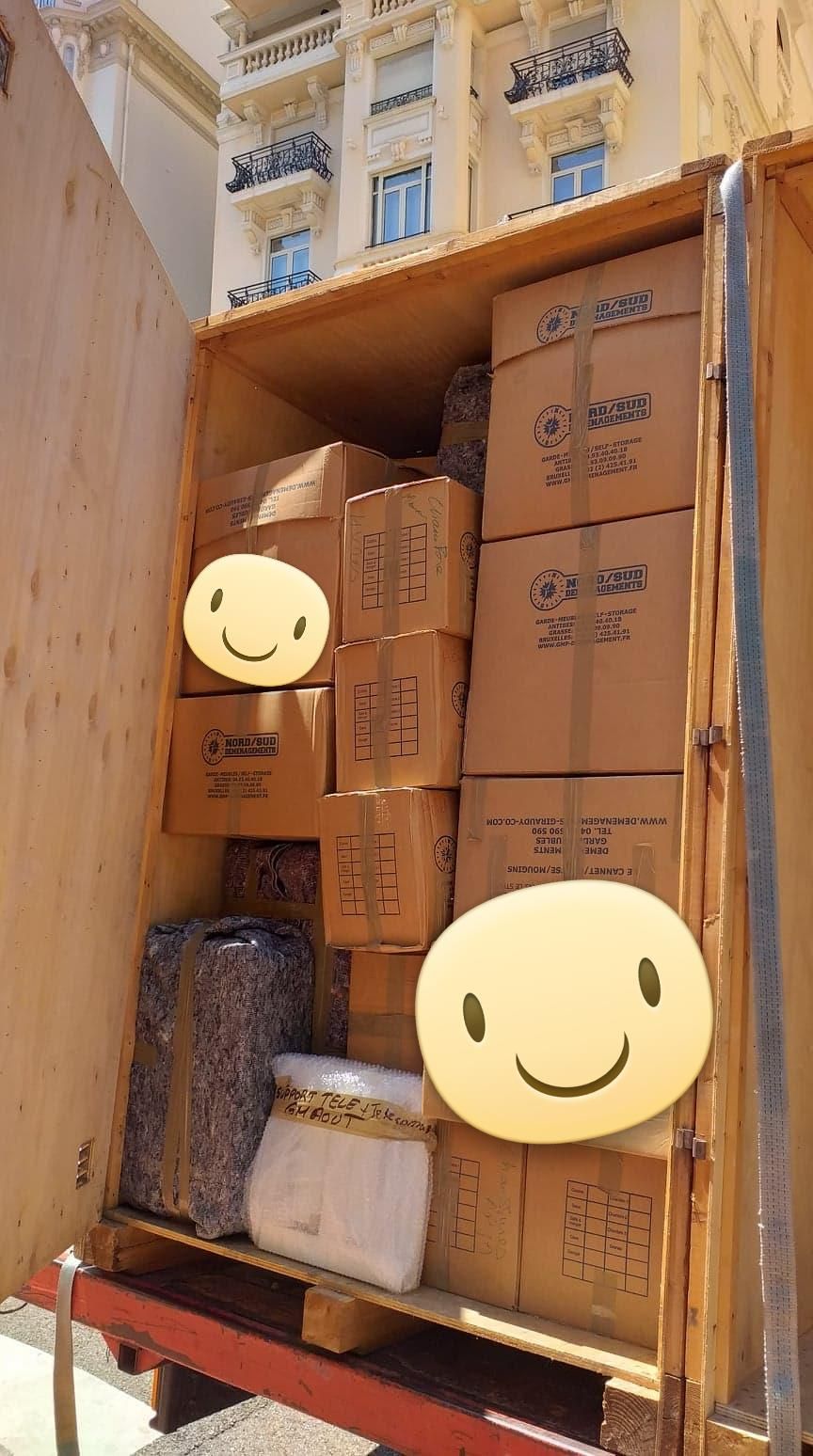Des cartons et des articles emballés empilés dans une caisse en bois, probablement pour un envoi ou un déménagement.
