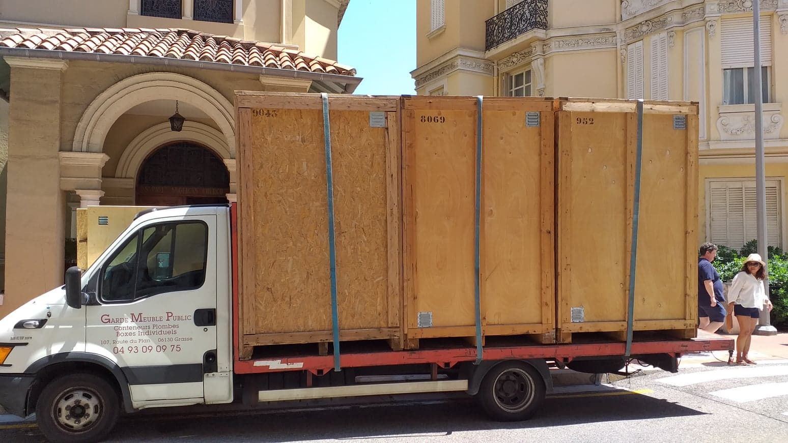 Camion transportant de grandes caisses en bois stationné dans la rue, passants en arrière-plan.