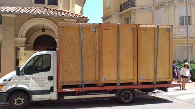 Camion transportant de grandes caisses en bois stationné dans la rue, passants en arrière-plan.