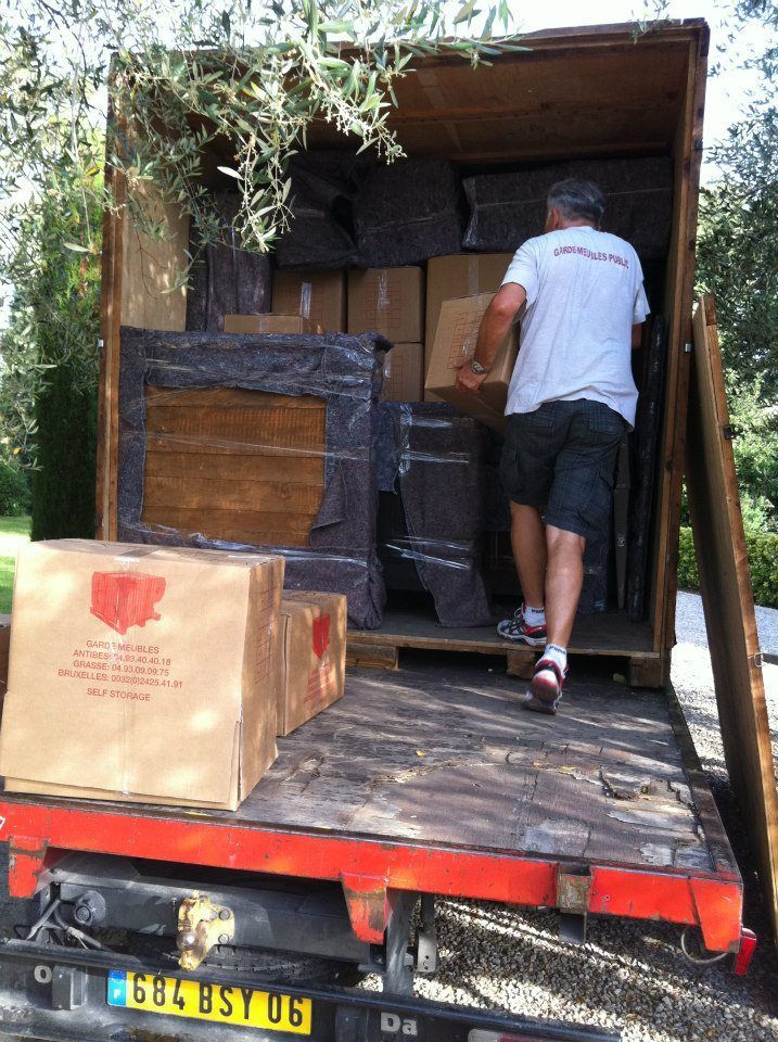 Un homme charge des cartons et des dalles de pierre dans la benne d'un camion. En extérieur, en journée.