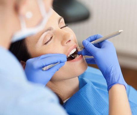 Dentista con guantes azules examinando la boca de un paciente con instrumental dental.