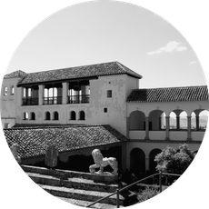 Fotografía en blanco y negro de un edificio con balcón, arcos y una estatua, probablemente en España.