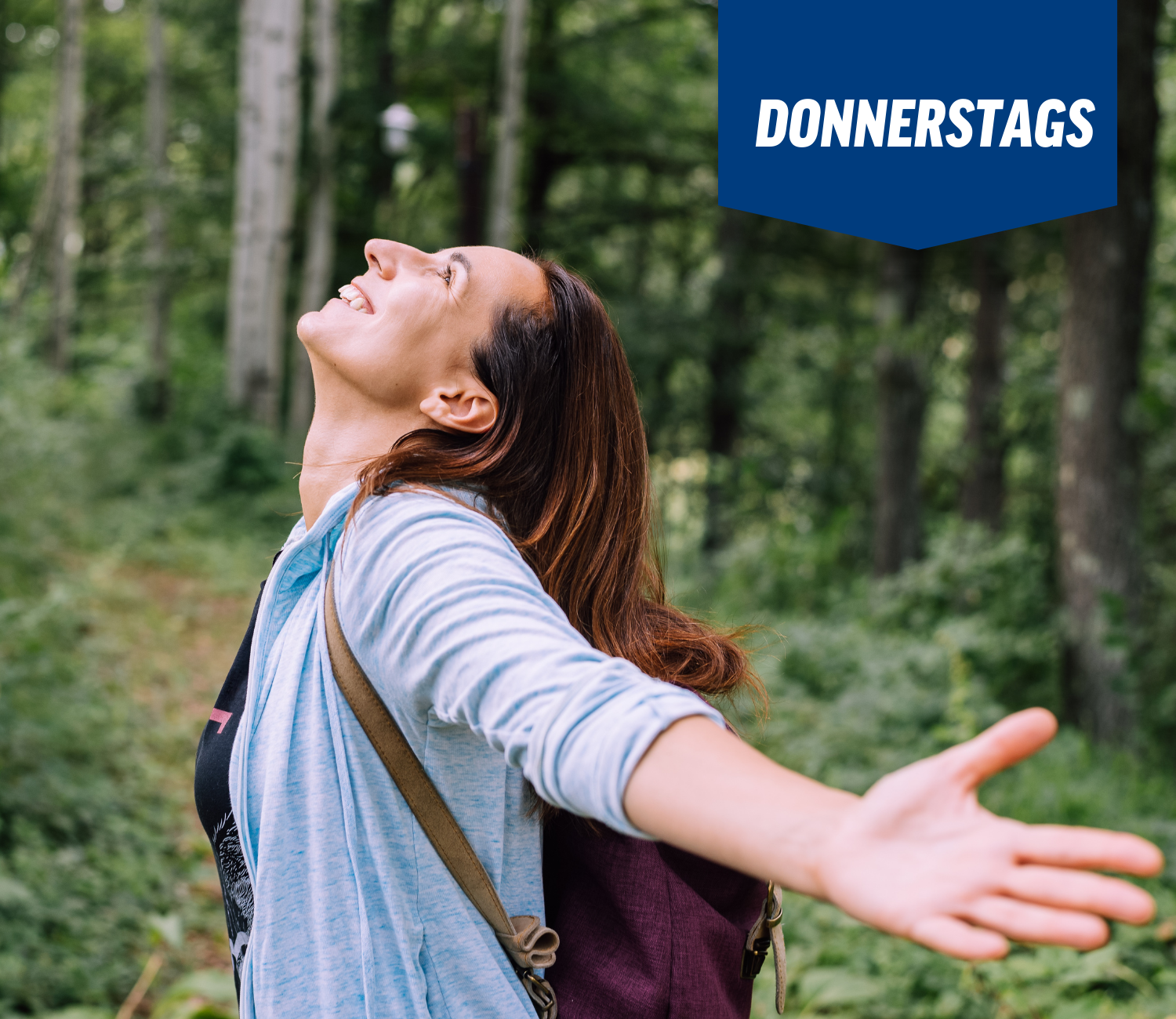 Eine Frau steht mit ausgestreckten Armen im Wald.