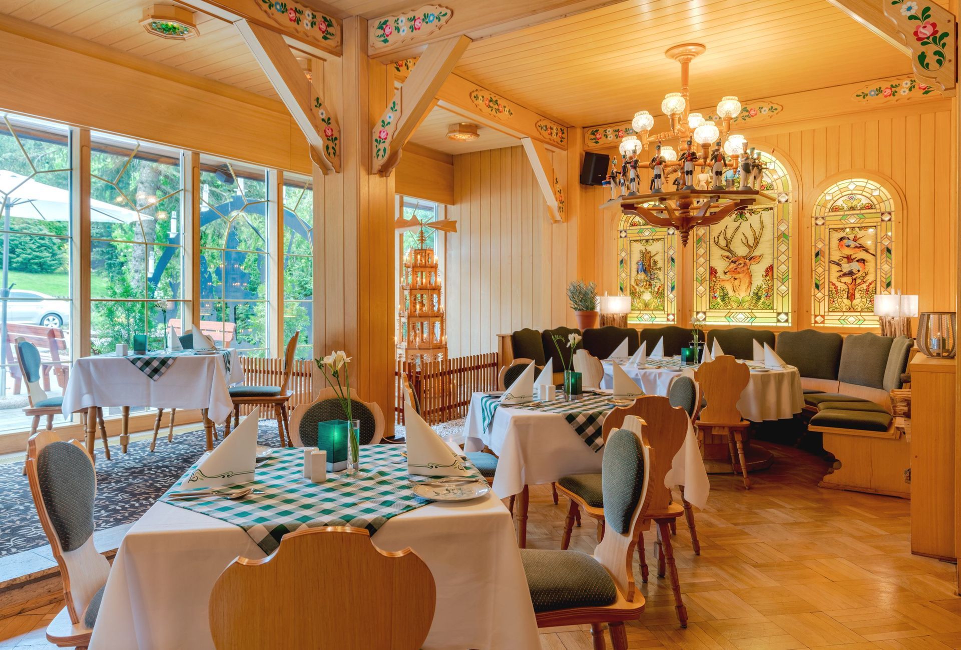 Elegantes Esszimmer mit weißen Tischdecken, Kronleuchtern und großen Fenstern mit Blick ins Grüne