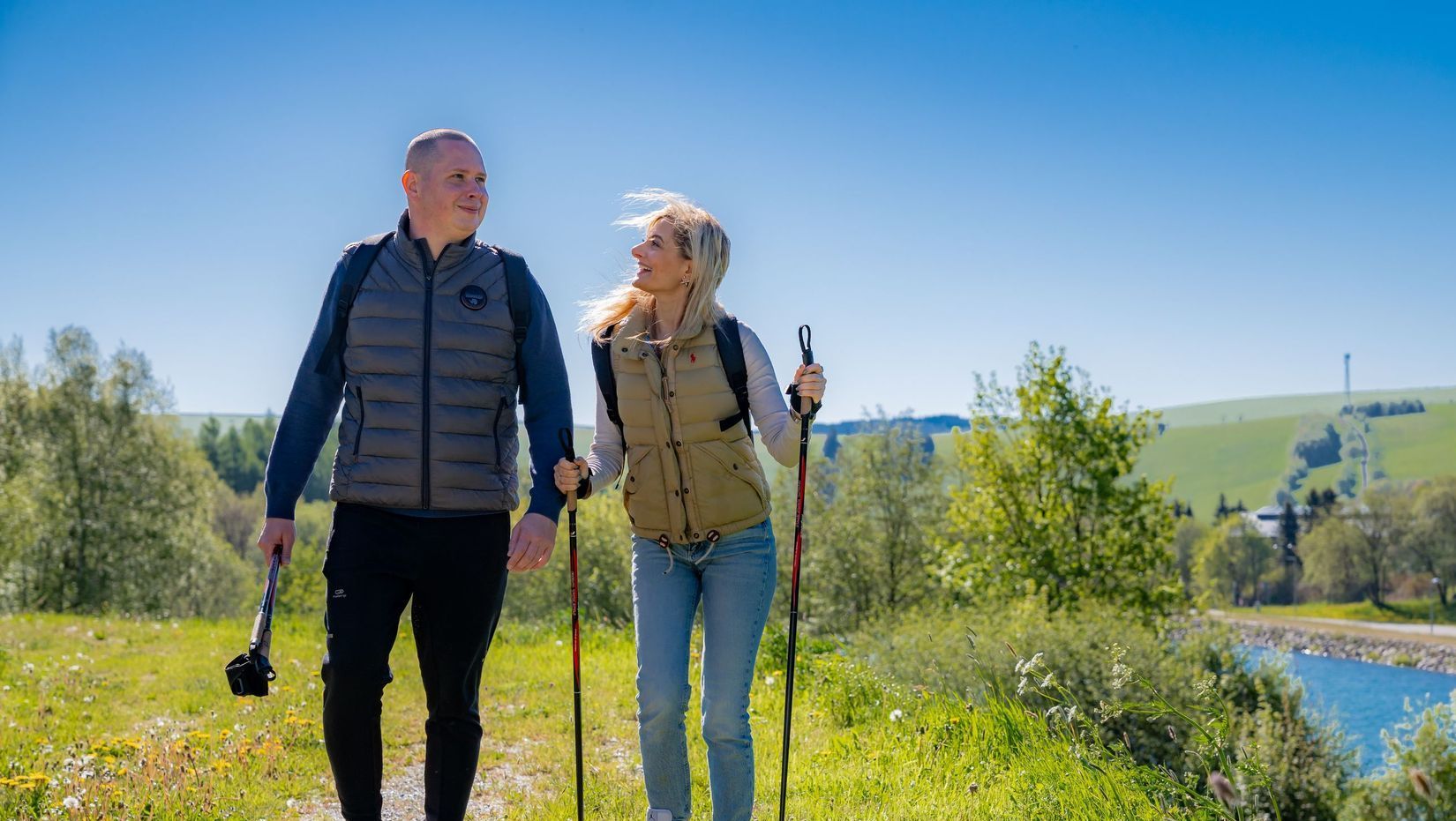 Ein Mann und eine Frau gehen mit Wanderstöcken einen Hügel hinauf.