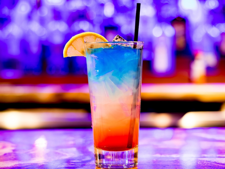 Ein bunter Cocktail mit einem Strohhalm und einer Zitronenscheibe auf einem Tisch.