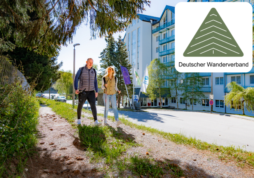 Zwei Personen gehen auf einer von Bäumen gesäumten Straße neben einem modernen Gebäude, in das das Logo des Deutschen Wanderverbands eingeblendet ist.