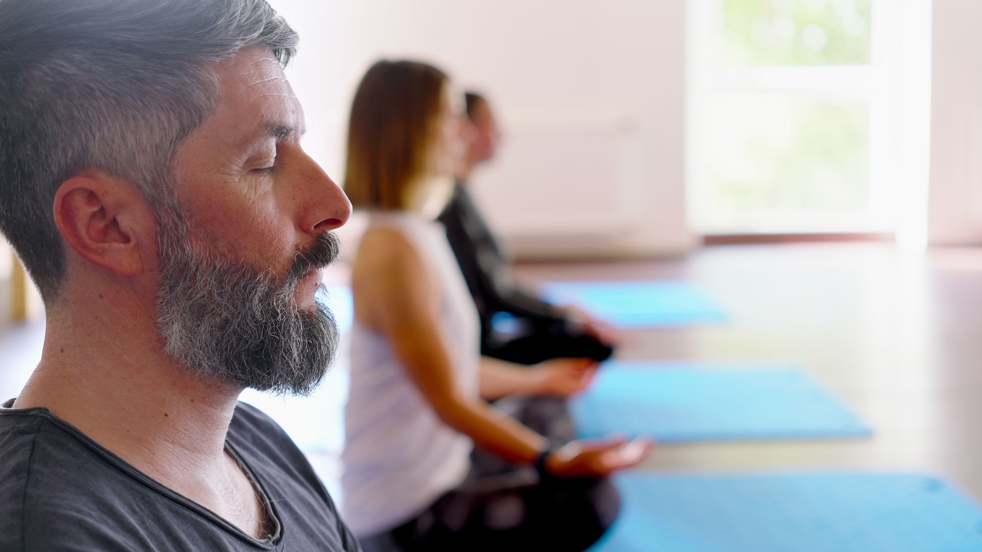 Eine Gruppe von Menschen sitzt mit geschlossenen Augen auf Yogamatten.
