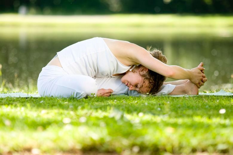 Eine Frau sitzt in einem Park auf einer Yogamatte im Gras.