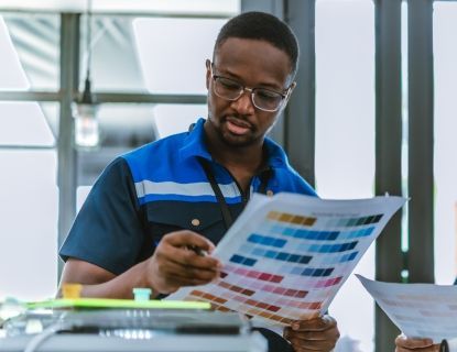Man examining a color chart in an office. He wears glasses and a blue collared shirt.