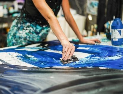 Artist using a tool to spread blue paint on a large canvas, creating an abstract design.