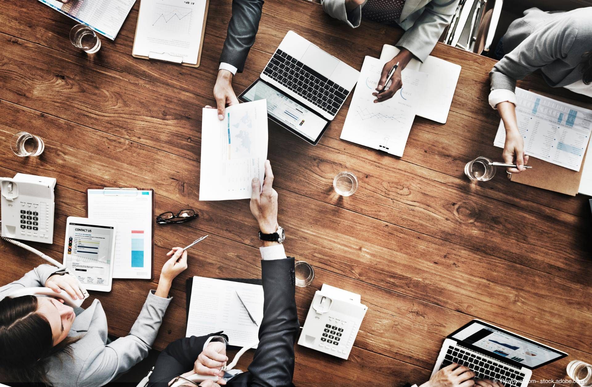 Mehrere Leute arbeiten und reichen sich Dokumente, Vogelperspektive.