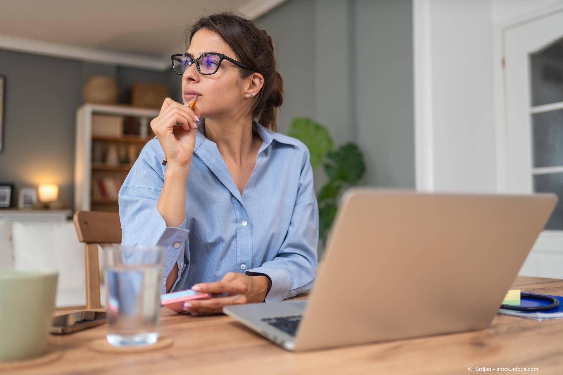 Eine Frau sitz nachdenkend vor einem Laptop.