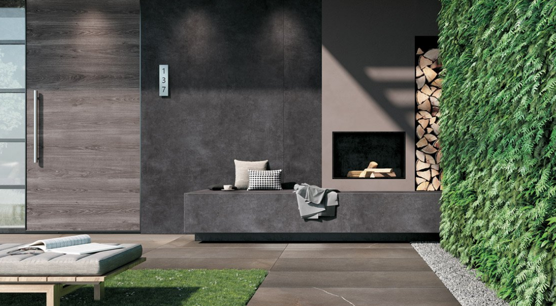 Terrasse moderne avec sièges gris, mur sombre, petite cheminée, bois de chauffage empilé et mur végétal vertical.