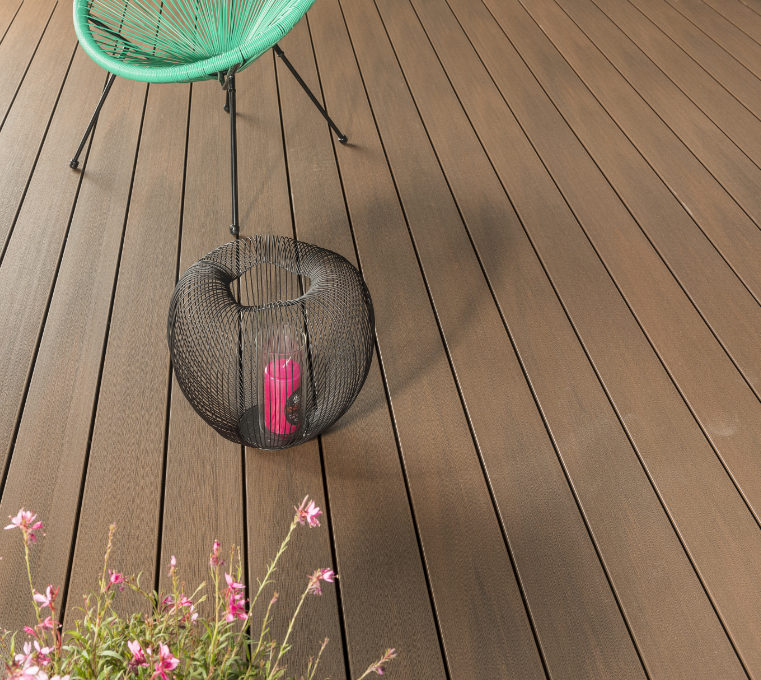 Jardinière suspendue noire avec une bougie rose sur une terrasse en bois, avec une chaise verte et des fleurs roses à proximité