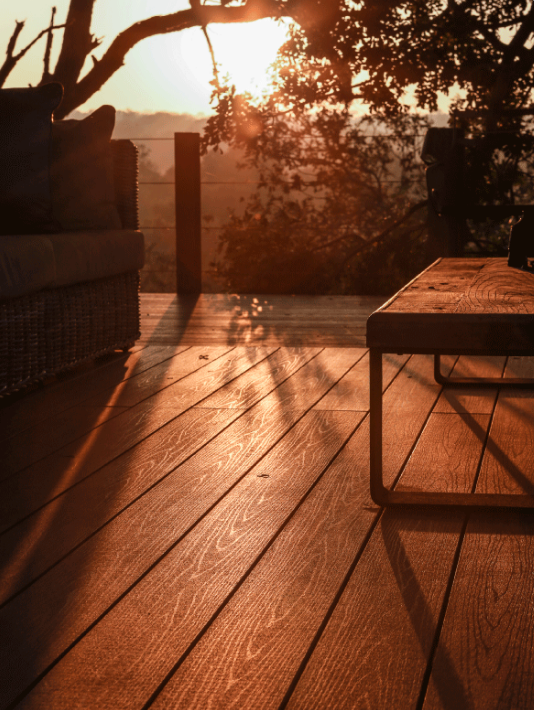 Terrasse en bois ensoleillée avec une table et une chaise en osier face à un coucher de soleil flou