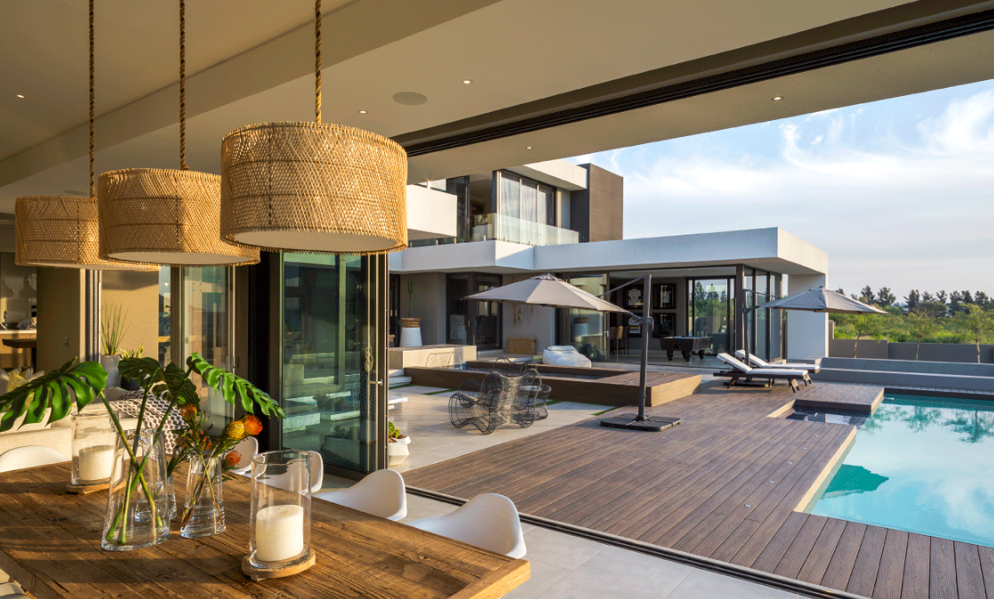 Terrasse luxueuse et moderne avec suspensions lumineuses en osier, salon de jardin et piscine donnant sur l'eau.
