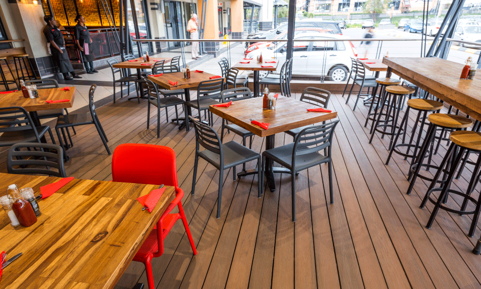 Terrasse de café extérieure vide avec tables en bois, chaises noires et chaises rouges vives
