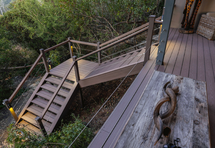Terrasse en bois avec escalier et rambarde descendant vers un flanc de colline boisé.