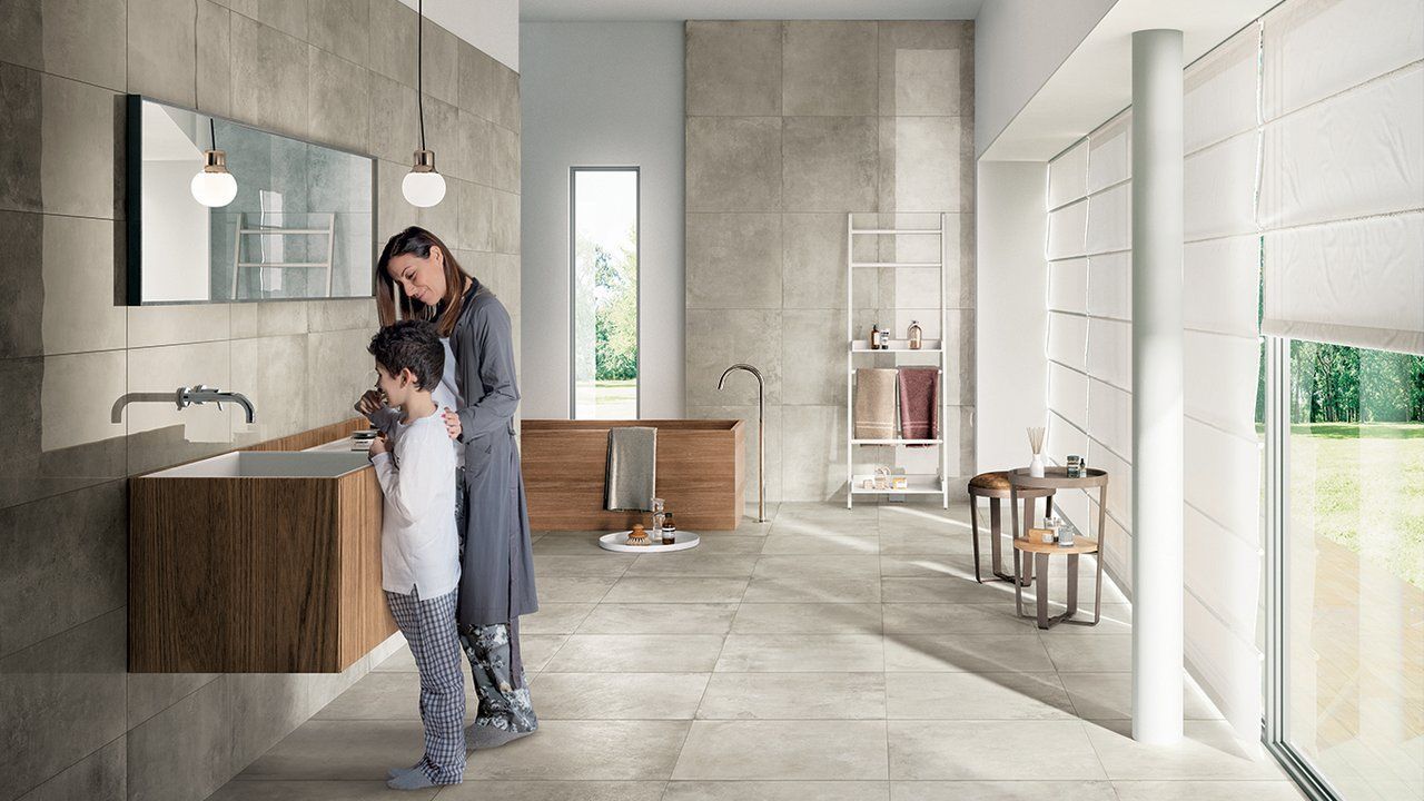 Un homme et un enfant se lavent les mains dans une salle de bains moderne aux carreaux gris et aux murs blancs.