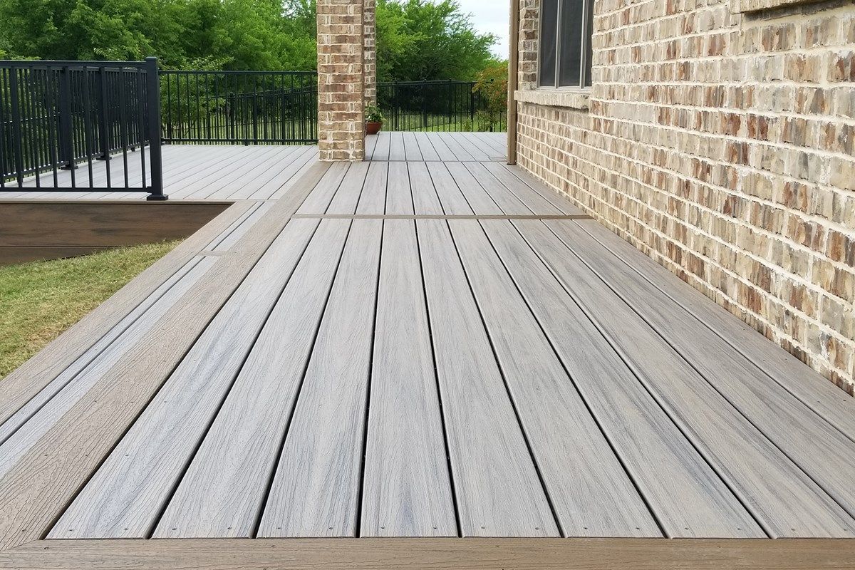 Terrasse en bois jouxtant une maison en briques avec une balustrade noire et des arbres verts au-delà