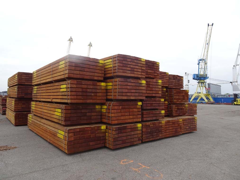 Des fagots de bois brun empilés dans une cour industrielle près d'une grue.
