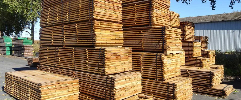 Des piles de bois soigneusement empilées à l'extérieur, sur un terrain vague sous les arbres