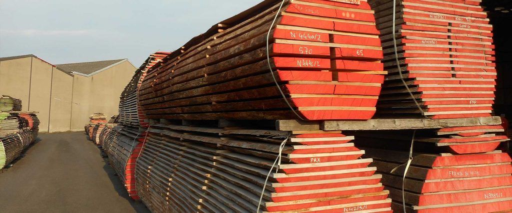 Des piles de poteaux en bois, aux extrémités peintes en rouge, empilés dans une cour extérieure